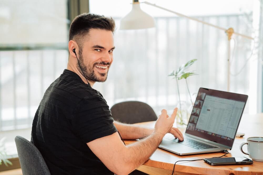 man with beard sitting smiling in front of laptop